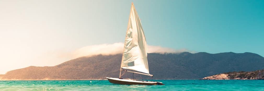 Sailing yacht with a big white sail on turquiose water with hills in the distance