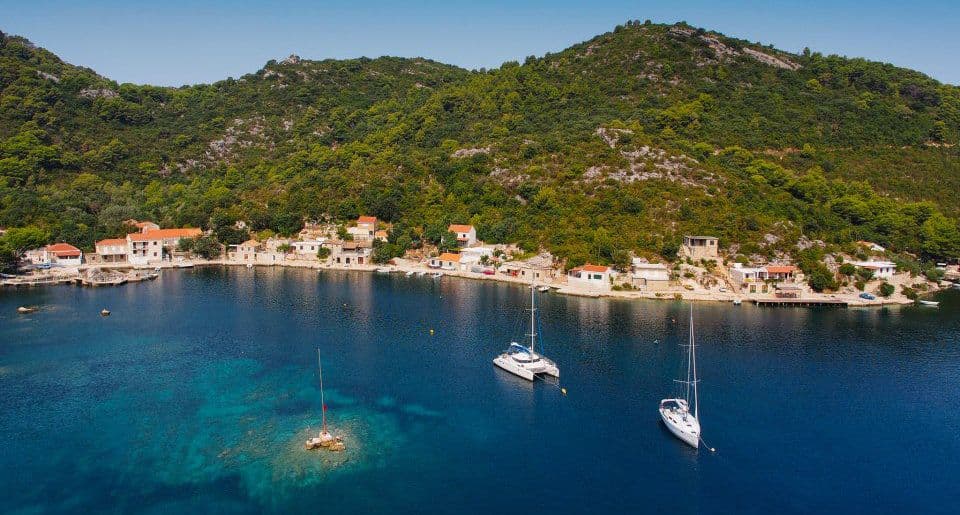 Two yachts on a water with small town and hills in the distance 