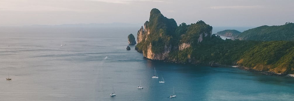 Big rock formation with yachts sailing on the water in front