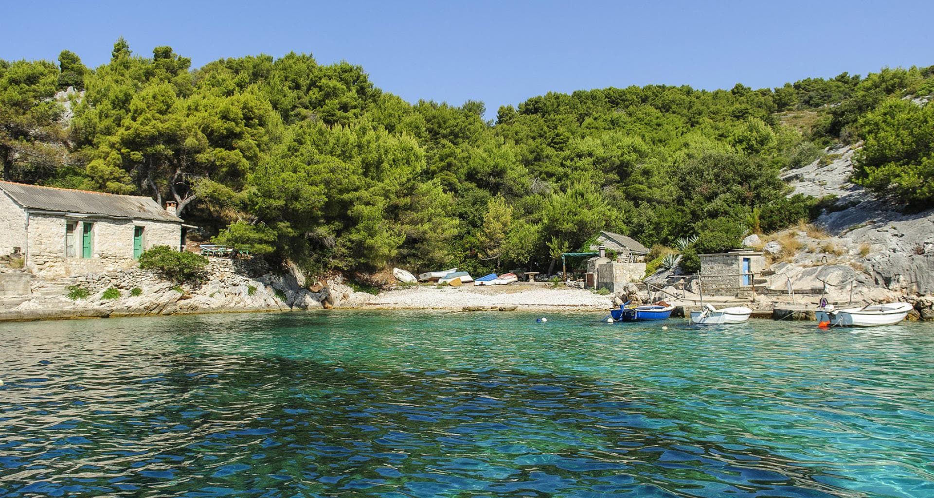 Secluded beach with greenery surrounding it and small boats on the water